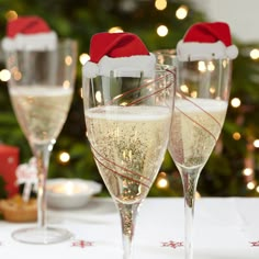 three wine glasses filled with champagne sitting on top of a table next to a christmas tree