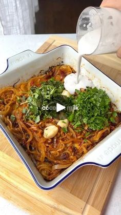 someone pouring milk on some noodles in a dish with parsley and cashews