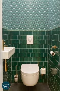 a bathroom with green tiles and gold fixtures on the wall, along with a white toilet and bidet