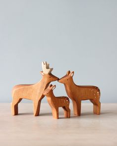 two wooden deer standing next to each other on top of a white table with a gray wall in the background