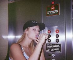 a woman is standing in front of an elevator and eating something out of her mouth