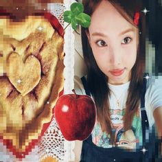 a girl is holding an apple and looking at the camera with a heart shaped pie in front of her