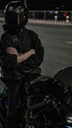 a man sitting on top of a motorcycle wearing a black jacket and helmet with his arms crossed