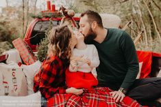 a man and woman kissing while sitting on a bed in front of a christmas tree