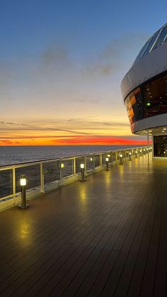 the deck of a cruise ship at sunset with lights on it's railings