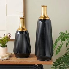 two black vases sitting on top of a wooden table next to a potted plant