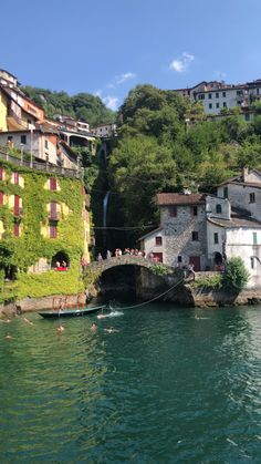 people are swimming in the water near some buildings and trees on top of a hill