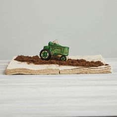 a green toy tractor sitting on top of a pile of dirt next to a book