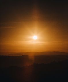 the sun is setting over some mountains and hills in the distance as seen from an airplane