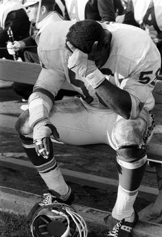 a football player kneels on the bench while holding his foot in one hand and looking down