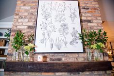 a brick fireplace with vases filled with flowers on the mantel and an art piece above it