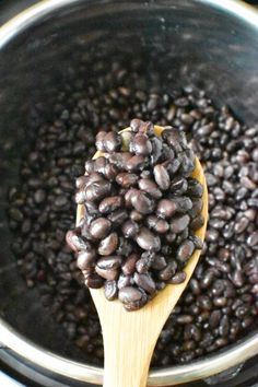 a wooden spoon filled with black beans on top of an instant pot full of water