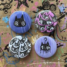 three buttons with designs on them sitting on top of a piece of graffiti covered paper