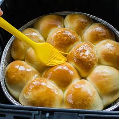 a person holding a yellow spatula in a pan filled with rolls