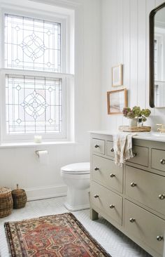 a white bathroom with stained glass window above the toilet and vanity area, along with a rug on the floor