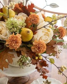 a white vase filled with lots of flowers on top of a wooden table next to plates