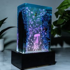 an illuminated jellyfish in the water on a marble countertop next to potted plants