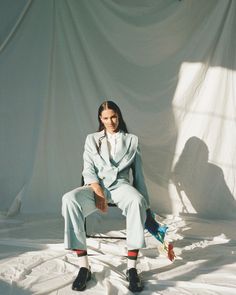 a person sitting on a chair in front of a white backdrop wearing a suit and socks