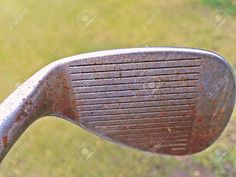 an old iron golf club with rust on it's side and grass in the background