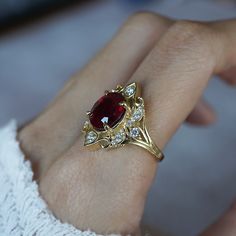 a woman's hand holding a ring with a red stone and white diamonds on it