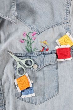 scissors and thread are sitting in the pocket of a jean jacket with embroidered flowers on it