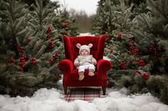 a baby sitting in a red chair surrounded by christmas trees