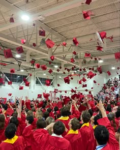 graduates in red caps and gowns toss their caps into the air as they celebrate