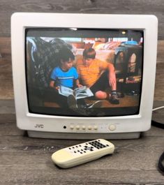 an old tv sitting on top of a wooden table next to a remote control and cords