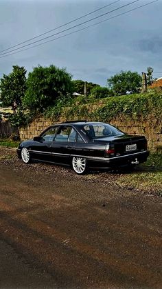 a black car parked on the side of a road next to a stone wall and grass