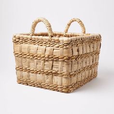 a woven basket with two handles on the top and one handle at the bottom, against a white background