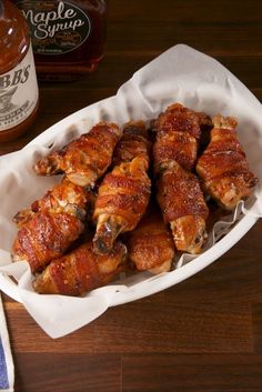 some chicken wings are in a basket on a table next to a bottle of maple syrup