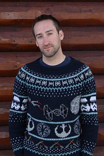 a man standing in front of a wooden wall wearing a star wars sweater and looking at the camera