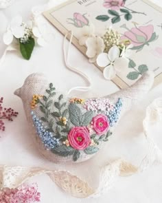 an embroidered bird with flowers on it sitting next to some lace and other things that are laying around