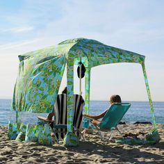 two people sitting in lawn chairs under a tent on the beach next to the ocean