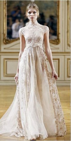 a model walks down the runway in a white gown with sheer lace detailing and high neck