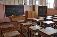 an empty classroom with wooden desks and chalkboard