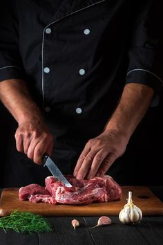 a chef cuts up raw meat on a wooden cutting board with garlic and parsley