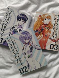 three anime book covers laying on top of a white bed sheet with an image of two women and one man