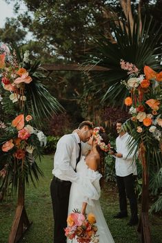 a bride and groom kissing under an arch decorated with tropical flowers at their wedding ceremony