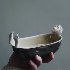 a hand holding a ceramic bowl with a small statue in the center and feet sticking out