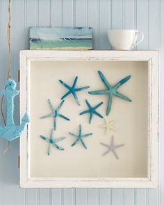 four starfishs are hanging in a frame on the wall next to a cup