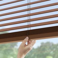 a hand is holding the blinds in front of a window with brown wood slats