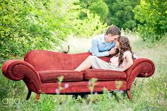 a man and woman sitting on top of a red couch in the middle of a field