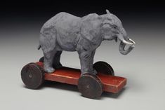 an elephant figurine sitting on top of a wooden toy wagon with wheels and two large tusks