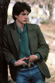 a man standing next to a tree wearing a green shirt and blazer with his hands in his pockets