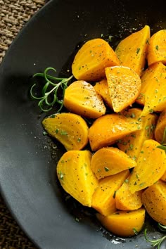 a black bowl filled with sliced up yellow squash and garnished with fresh herbs