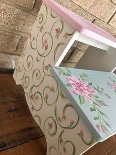 a pink and blue shelf with flowers painted on the top, next to a brick wall