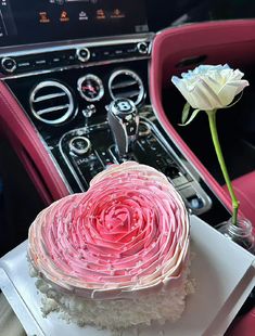 a pink and white cake sitting on top of a plate next to a car steering wheel