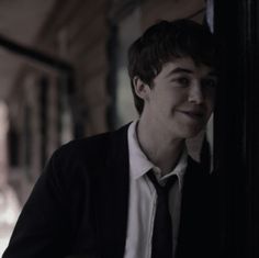 a young man wearing a suit and tie leaning against a wall with his hand on the door