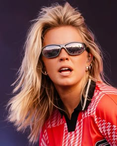 a woman with sunglasses on her face and hair blowing in the wind while wearing an orange jacket